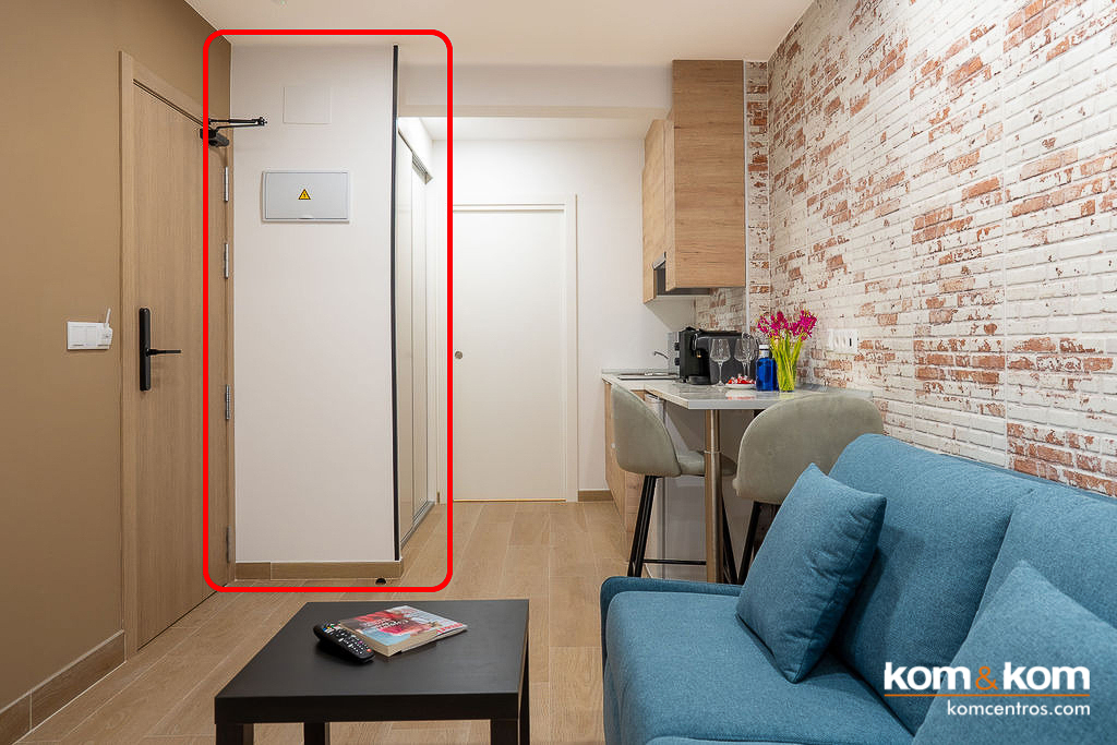 Armario empotrado a medida con puertas correderas en acabado blanco liso, dise&ntilde;ado por Kom&Kom para maximizar el aprovechamiento de espacio en la entrada de apartamentos tur&iacute;sticos Emily Suits.